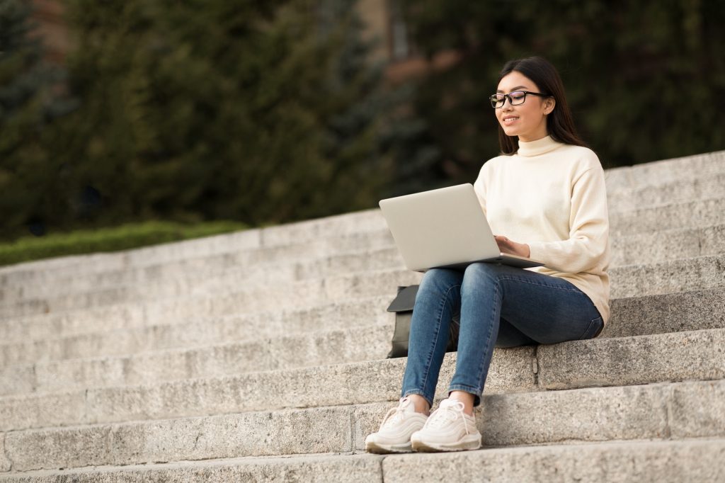 Student in specs using laptop, sitting on steps